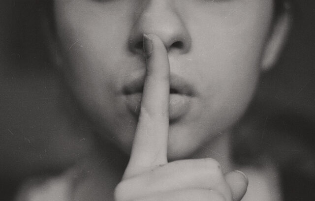 Woman pressing finger to lips representing confidentiality