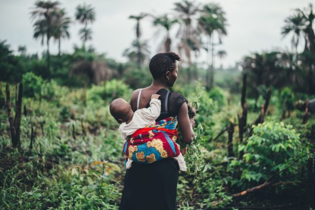 Woman with baby on her back in vegetation presumably in Nigeria