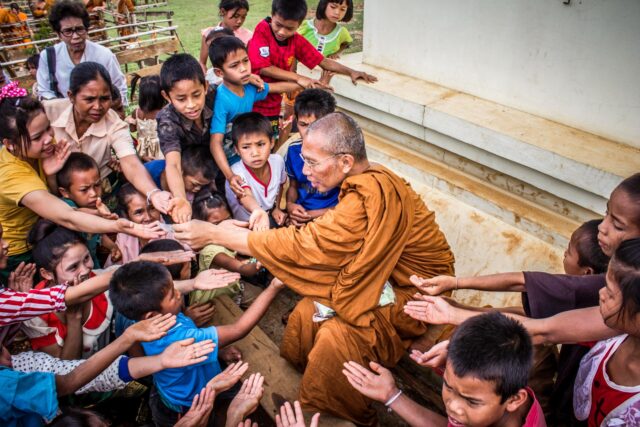 A compassionate monk offering things to group of surrounding children