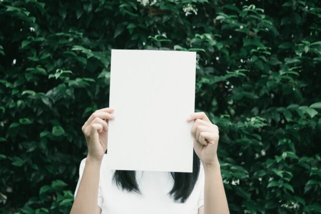 Woman holding paper blocking her face representing personality in conflict