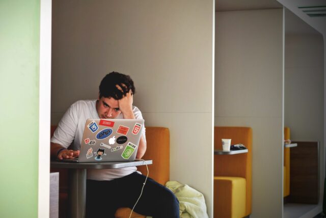 Man in the software industry at a cubbied table stressed with his computer