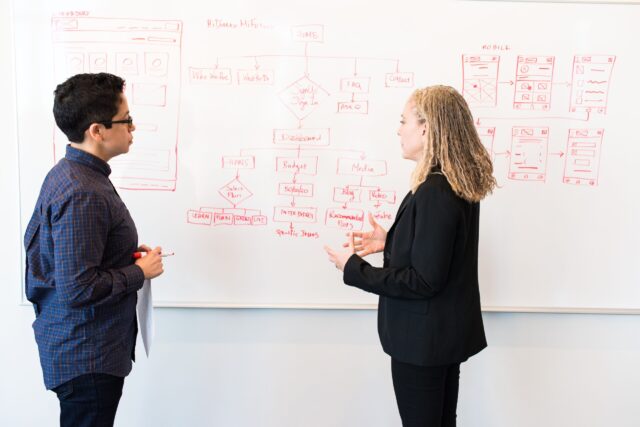 Two women drawing on white board planning how to prevent workplace interpersonal conflict