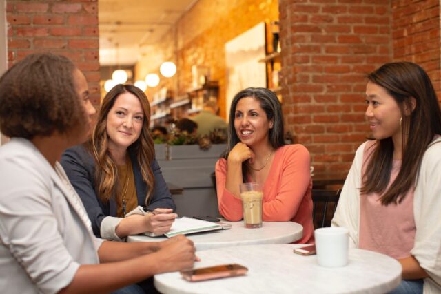 Professional women sitting at a table discussing work in formal clothing and looking joyful because their need for connection is met.