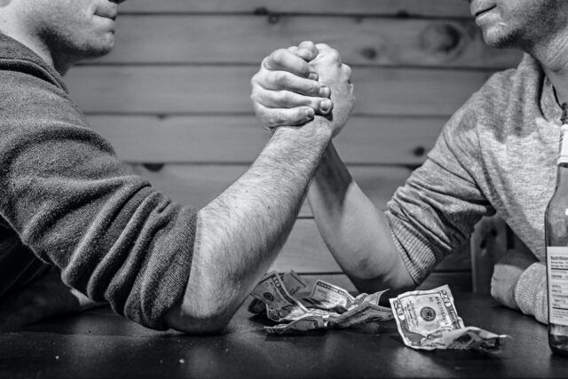 Two people arm wrestle over money, relating to competition for resources