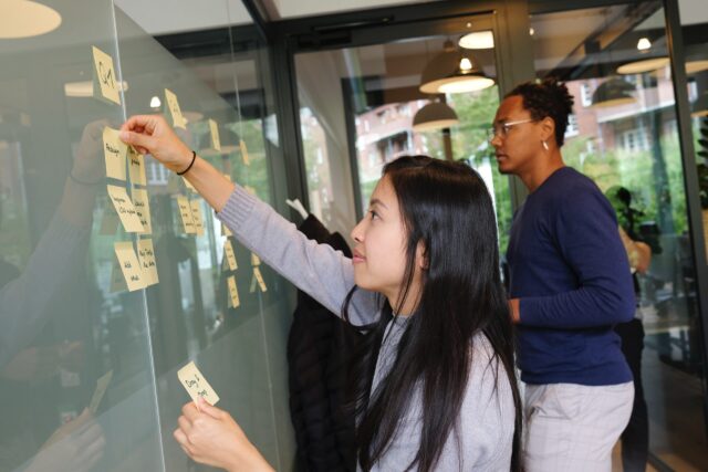 Two Millennial employees working putting post-it notes on a whiteboard