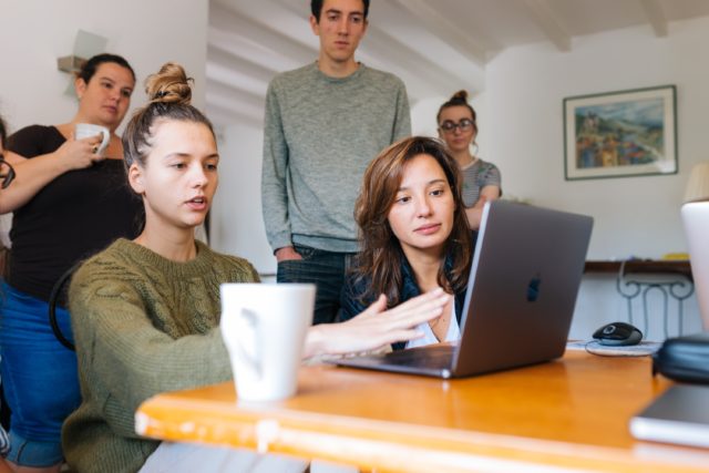 six employees gathered around a computer talking about conflict management