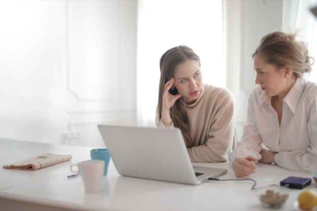 Two employees talking by a computer showing that resolving a conflict at work usually starts with communication