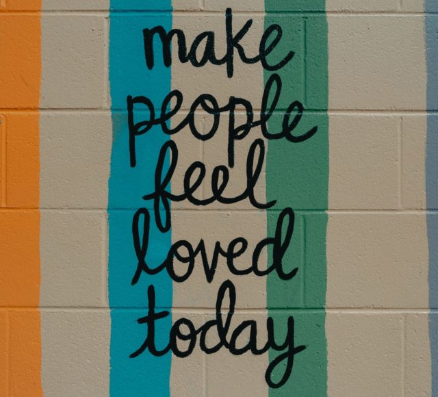 A painted wall that says "make people feel loved today" signifying empathy training