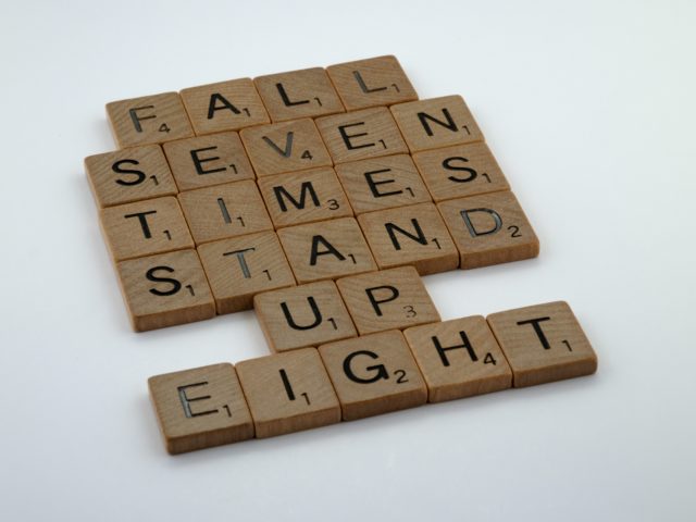 Scrabble pieces arranged to say "fall seven times stand up eight" symbolizing resilience