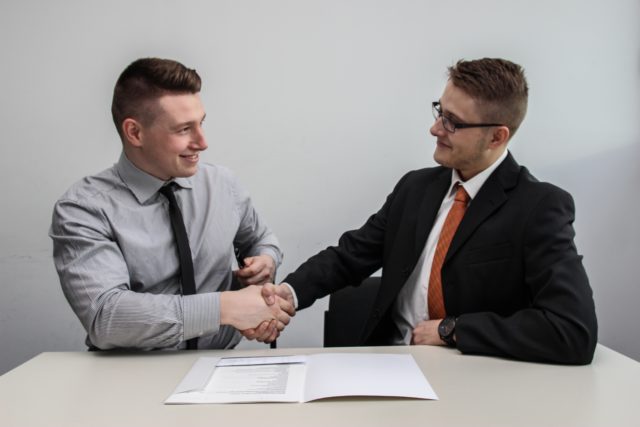 Two men in business attire shaking hands and smiling, showing Self-Control in the Workplace