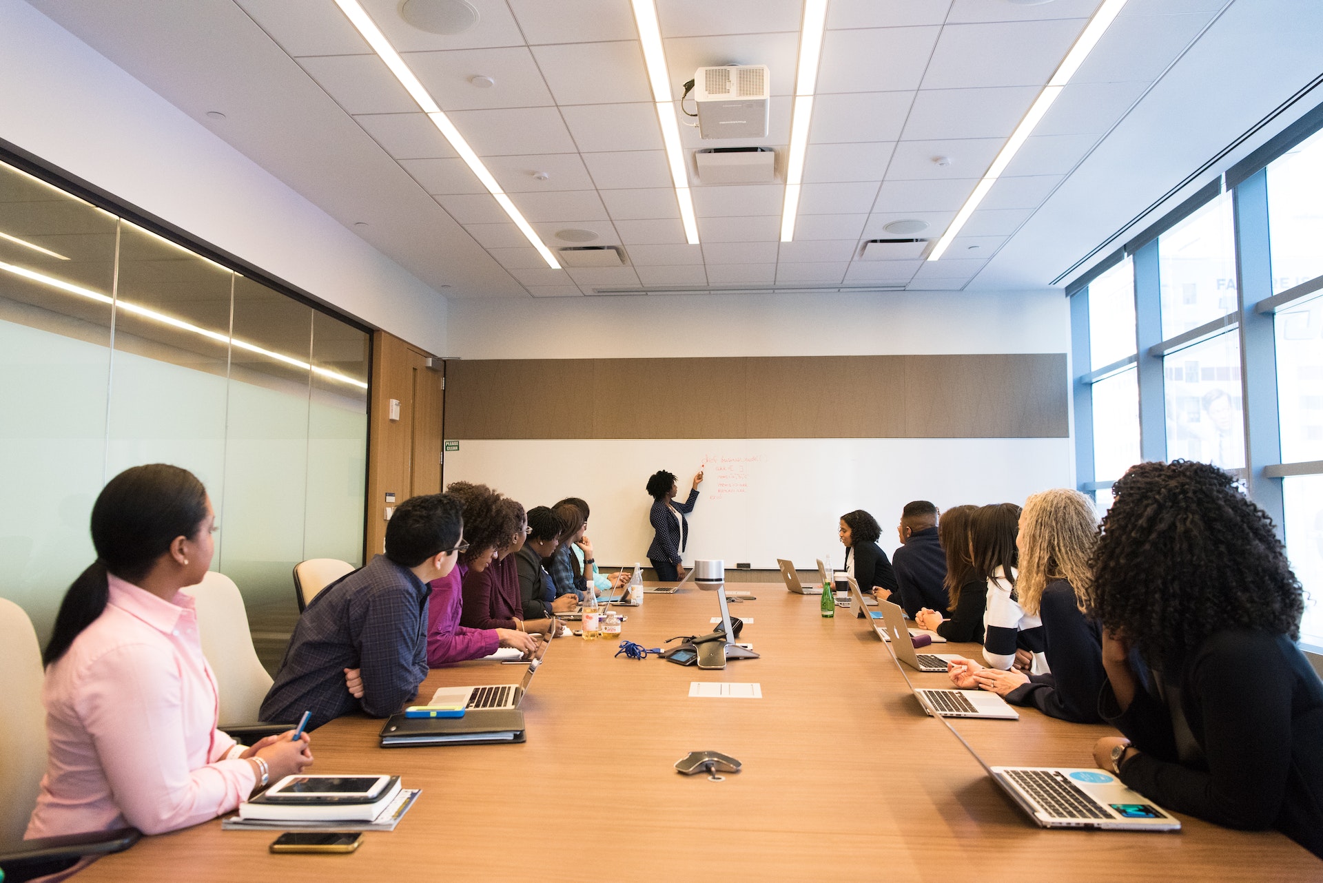 Training course where the trainees are seated at a desk and the trainer is writing on the whiteboard 