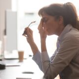 Tired woman at a computer desk holding her glasses