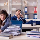 Busy businesswoman overwhelmed with work while her business partner is being lazy by talking on the phone