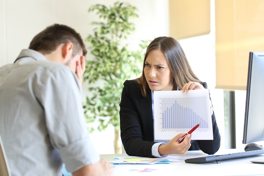 Angry woman showing a decreasing productivity graph to a lazy business partner