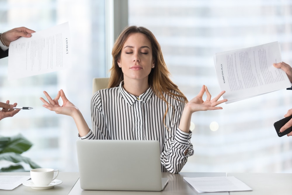 Calm female executive meditating taking break at work for mental balance, mindful businesswoman feeling relief and no stress doing yoga at work ignoring avoiding stressful job and paperwork in office