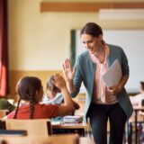 Happy elementary school teacher giving high-five to her student during class in the classroom.