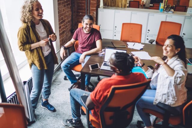 Group of young modern mutltiethnic employees chatting happily while sharing thoughts about new office.